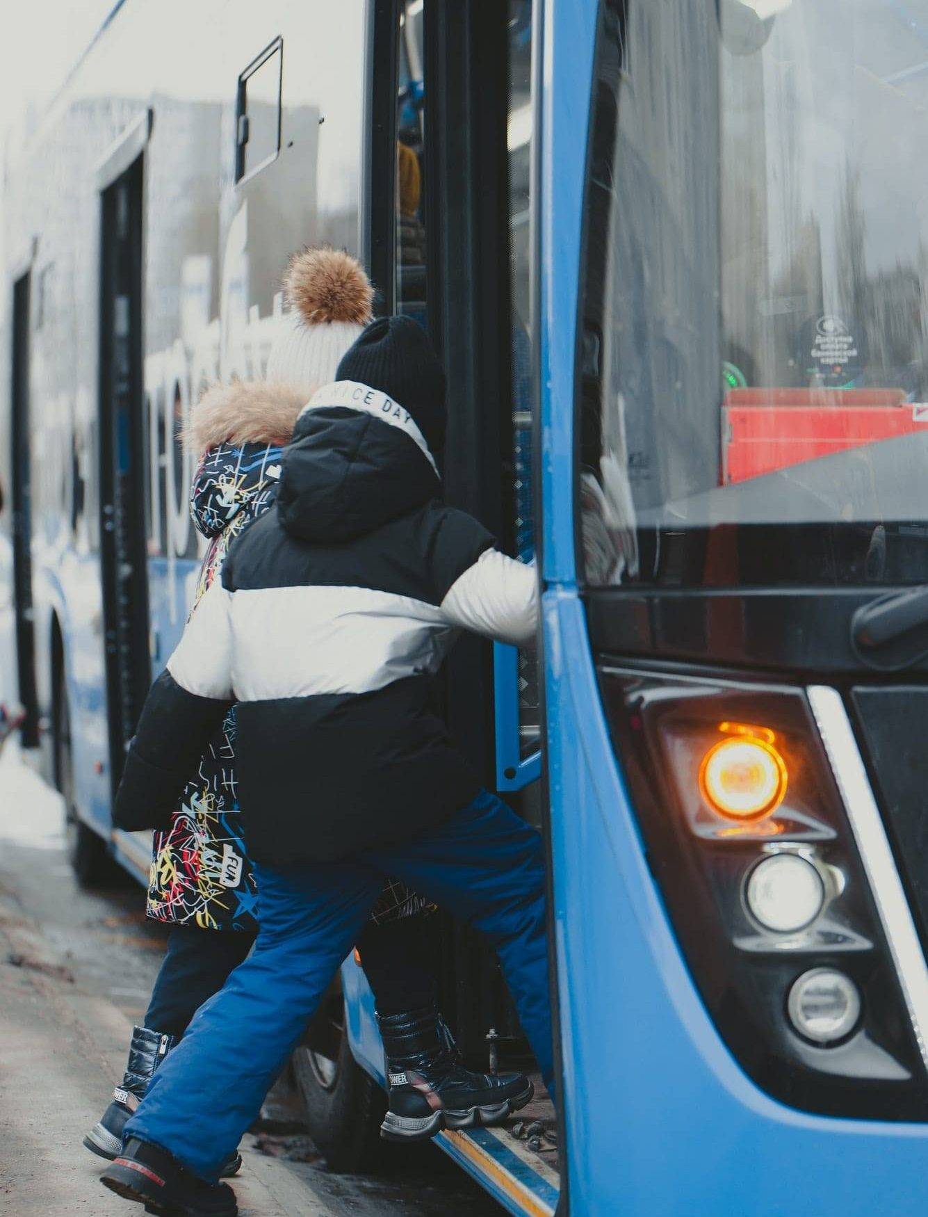 the-girls-enter-the-doors-of-a-blue-bus-that-has-arrived-at-the-bus-stop-.jpg two children getting off a bus